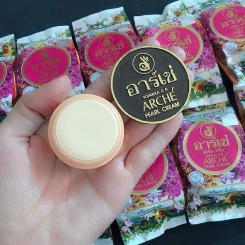 Hũ kem nhỏ đặt trên tay, thấy rõ nắp đen chữ vàng và chất kem sáng màu