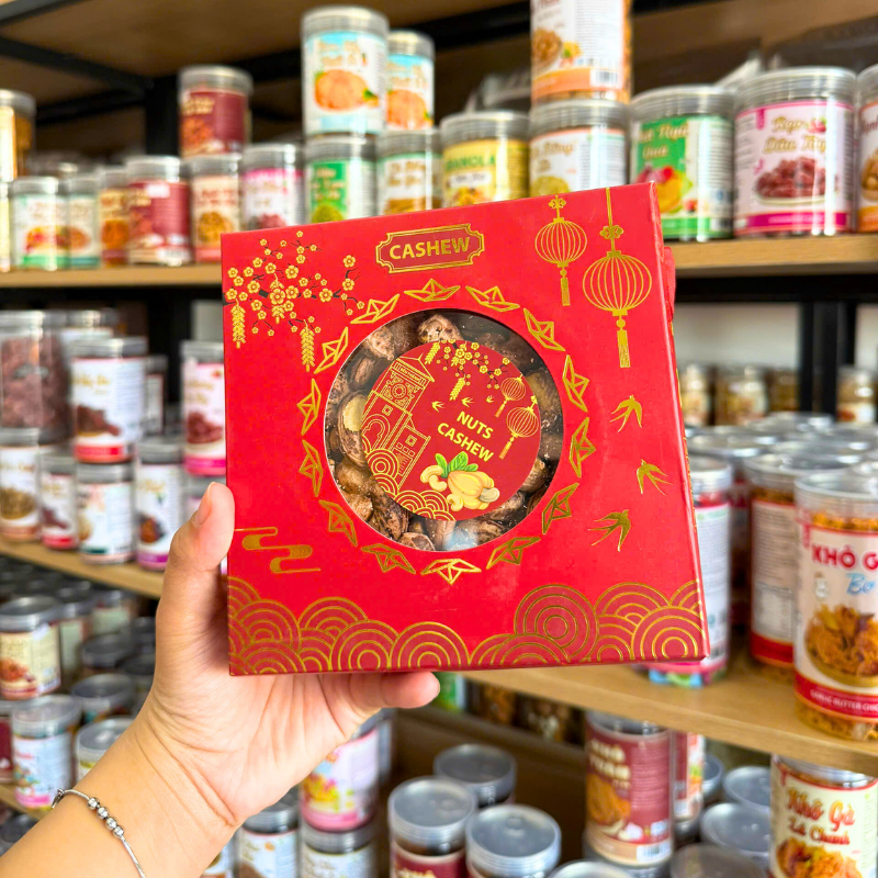 Mặt trước hộp đỏ ánh kim, cửa sổ tròn nhìn thấy hạt điều bên trong