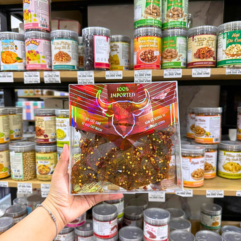 Miếng khô bò phủ gia vị và hạt ớt nhìn rõ qua mặt hộp trong