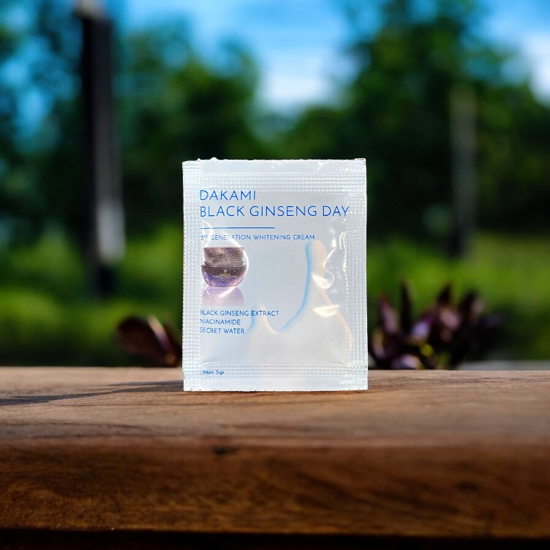 Gói DAKAMI BLACK GINSENG DAY dựng trên mặt gỗ, nền cây xanh mờ.