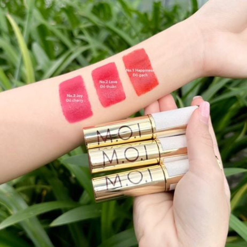 Ba thỏi ánh kim chữ M.O.I đặt cạnh swatch màu trên cẳng tay