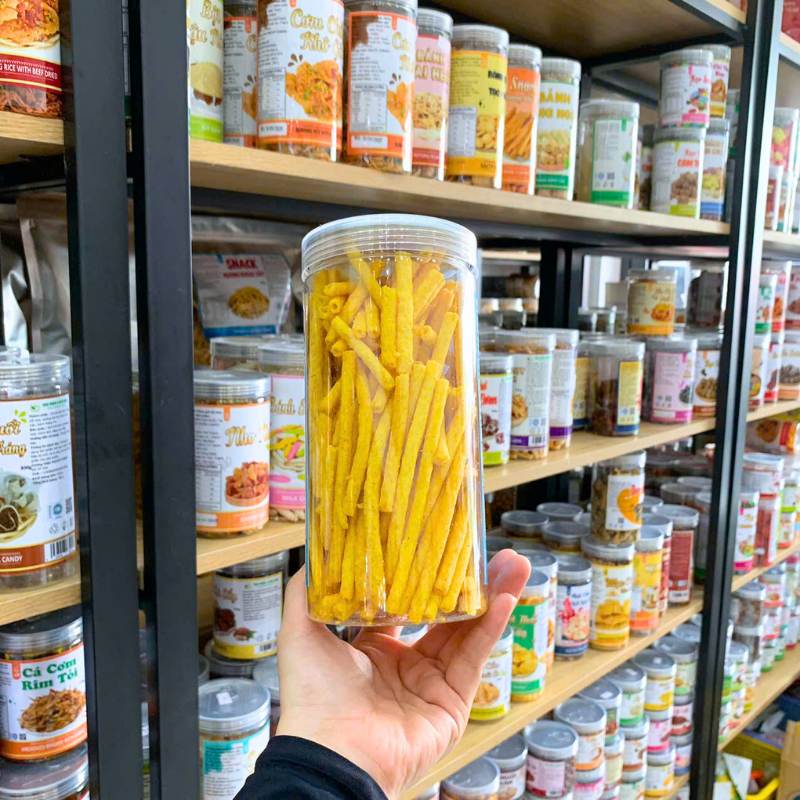 Cận cảnh snack dạng ống/que màu vàng trong hộp PET