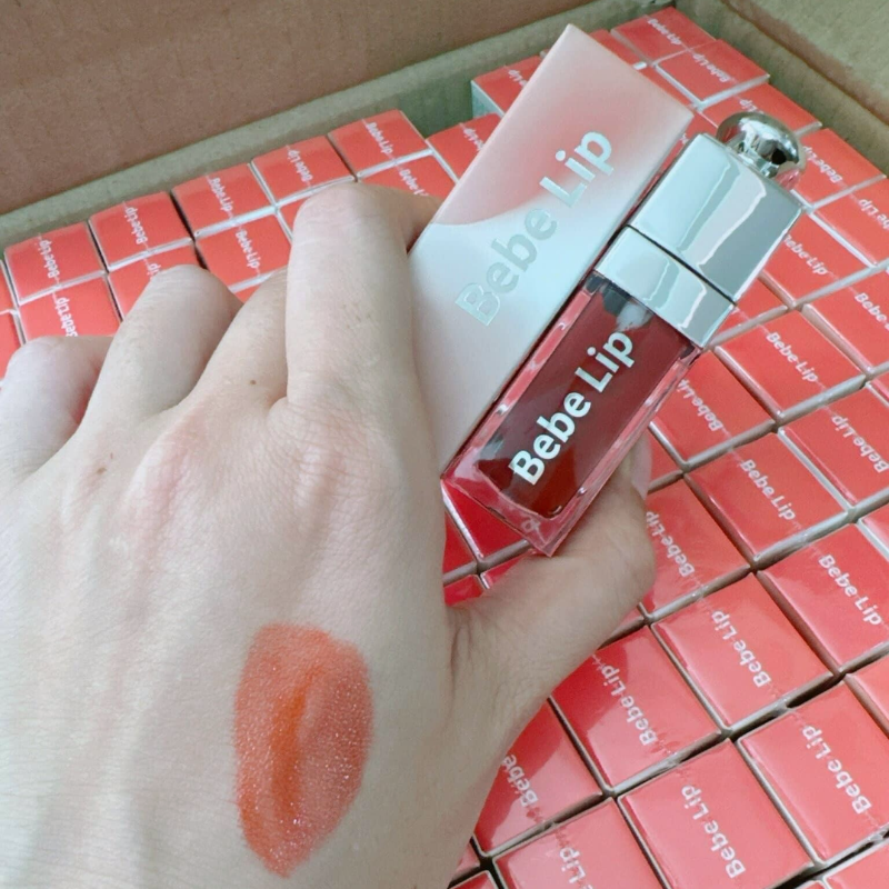 Vệt swatch đỏ cam cạnh thân son và hộp xếp nền phía sau